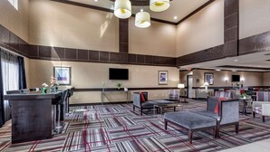 Een ruime lobby met een patroonrijk tapijt, zithoeken, een receptiebalie en een wandgemonteerde flatscreen-tv.