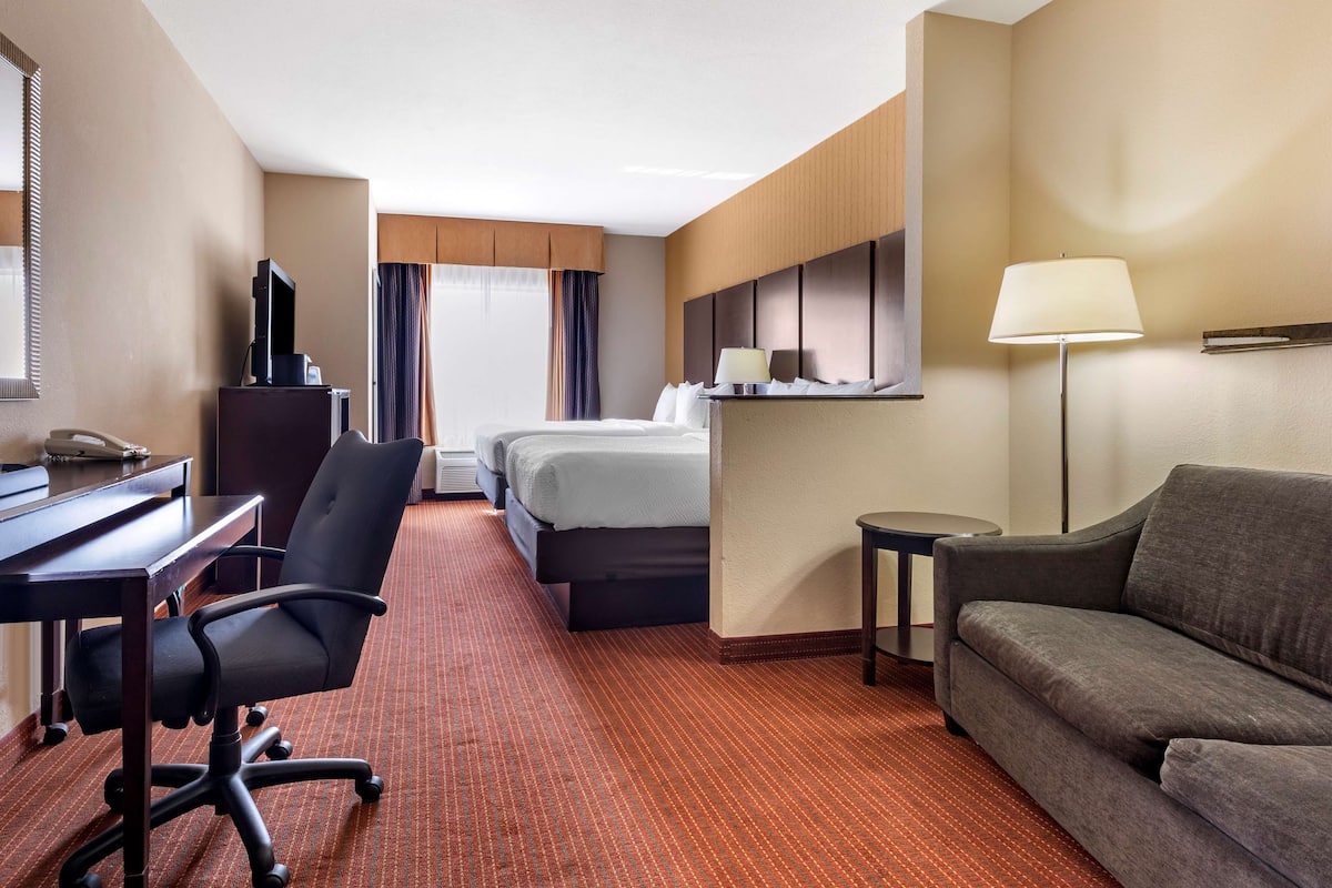 Habitación de hotel con cama, escritorio con computadora, silla, sofá, lámpara y televisor.