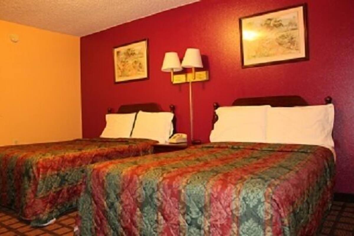 Ein Hotelzimmer mit zwei Betten, einem Nachttisch, einer Lampe und zwei gerahmten Bildern an der Wand.