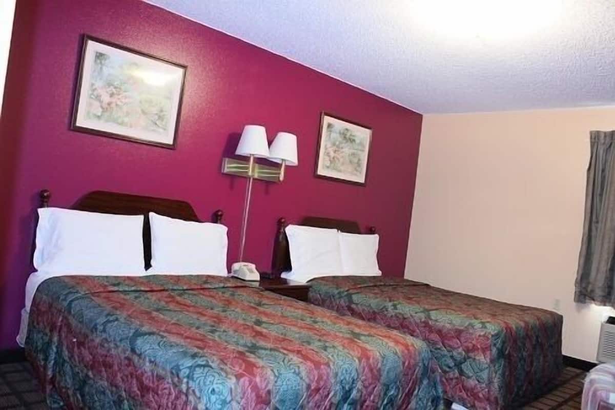 Ein Hotelzimmer mit zwei Betten, einem Nachttisch, einer Lampe und zwei gerahmten Bildern an der Wand.