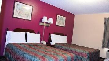 A hotel room with two beds, a nightstand, a lamp, and two framed pictures on the wall.