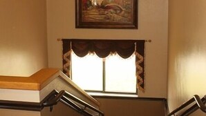 A staircase with a patterned carpet, a chandelier, and a framed painting above. - Holiday Lodge (Pittsburg)