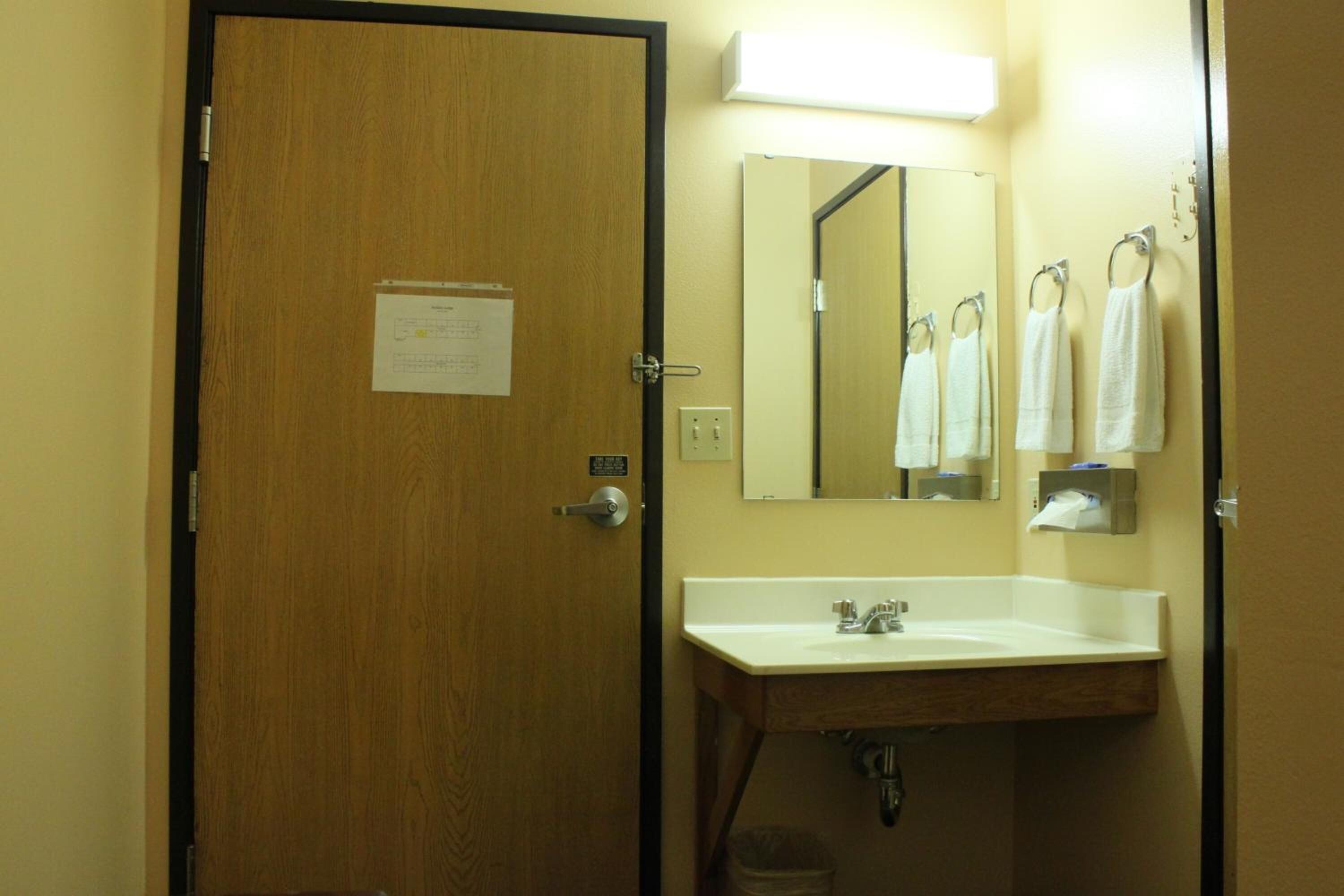 A bathroom with a wooden door, a white sink, a mirror, and several white towels hanging on hooks.