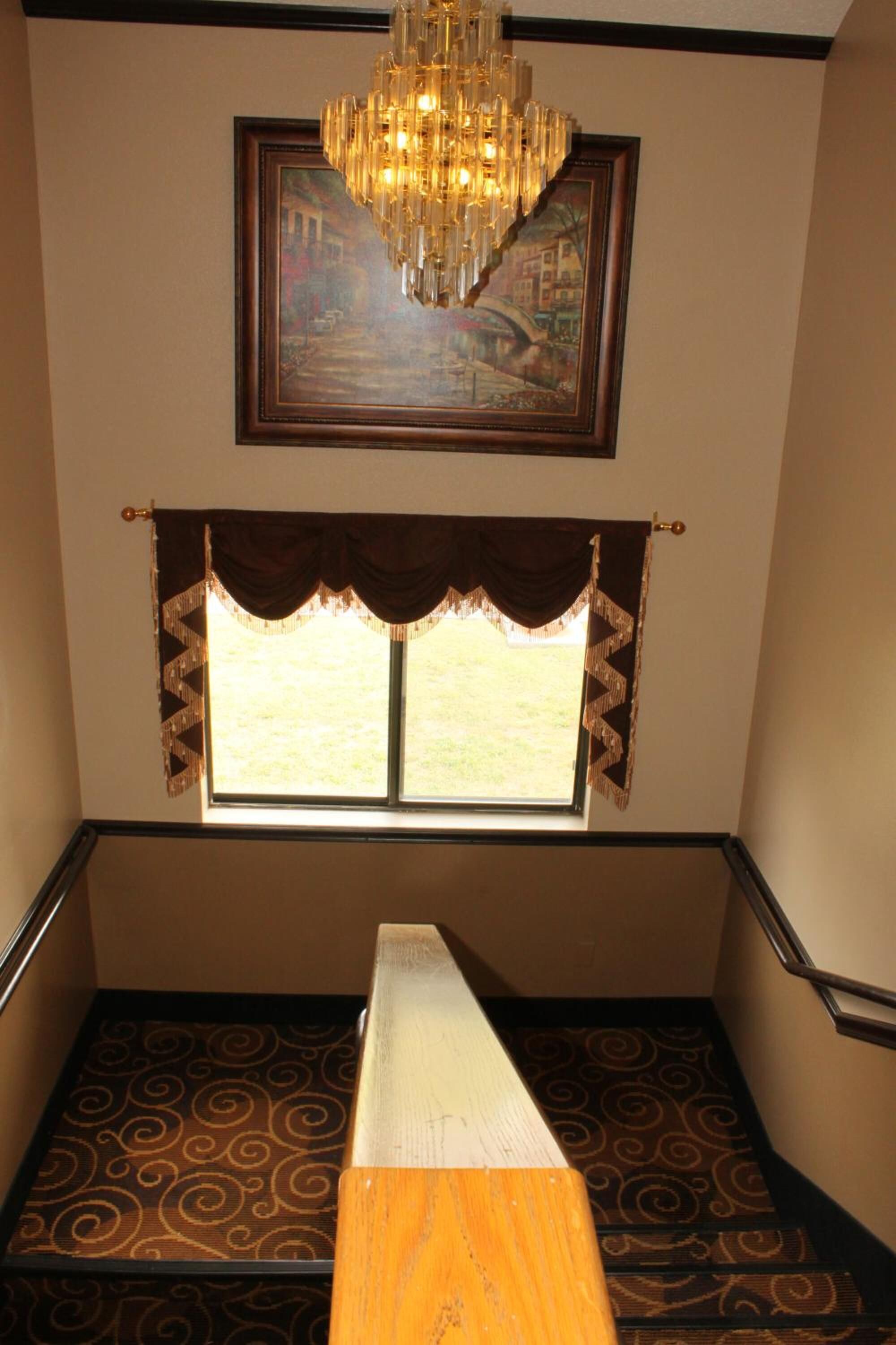 Una escalera con alfombra estampada, barandilla de madera, candelabro y un cuadro enmarcado arriba.