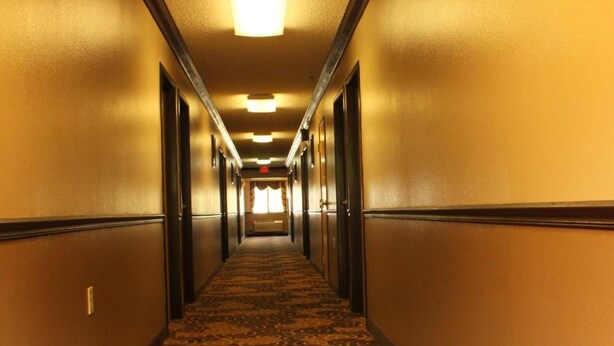 A hotel hallway with a patterned carpet, doors on both sides, and a light at the end. - Holiday Lodge (Pittsburg)