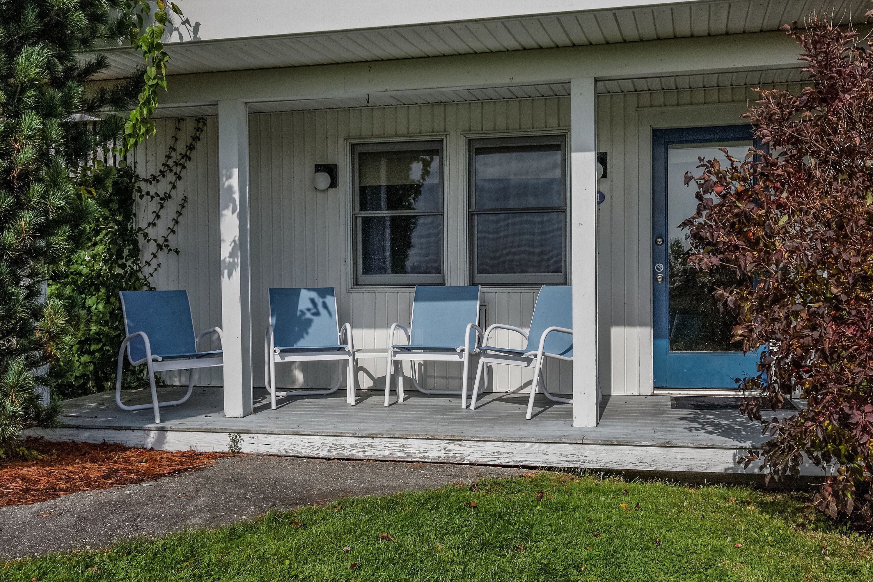A building with a porch, three chairs, and a blue door.