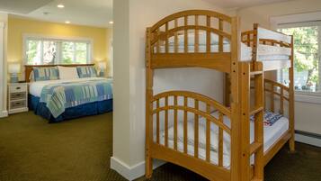 A bedroom with a bunk bed and a double bed, both with white bedding. There is a window with a view of greenery outside.