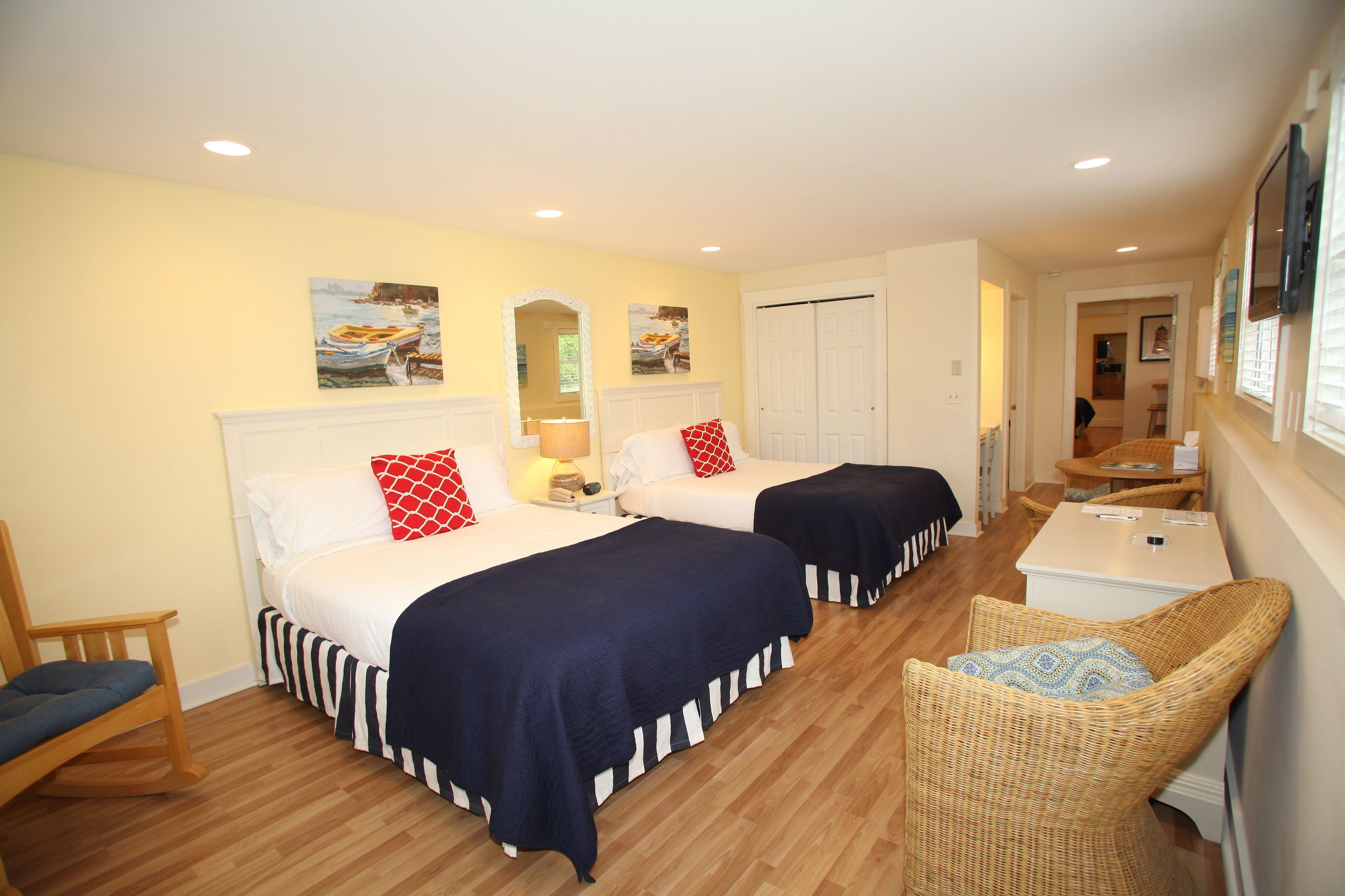 A hotel room with two beds, a small table, a chair, and artwork on the walls.