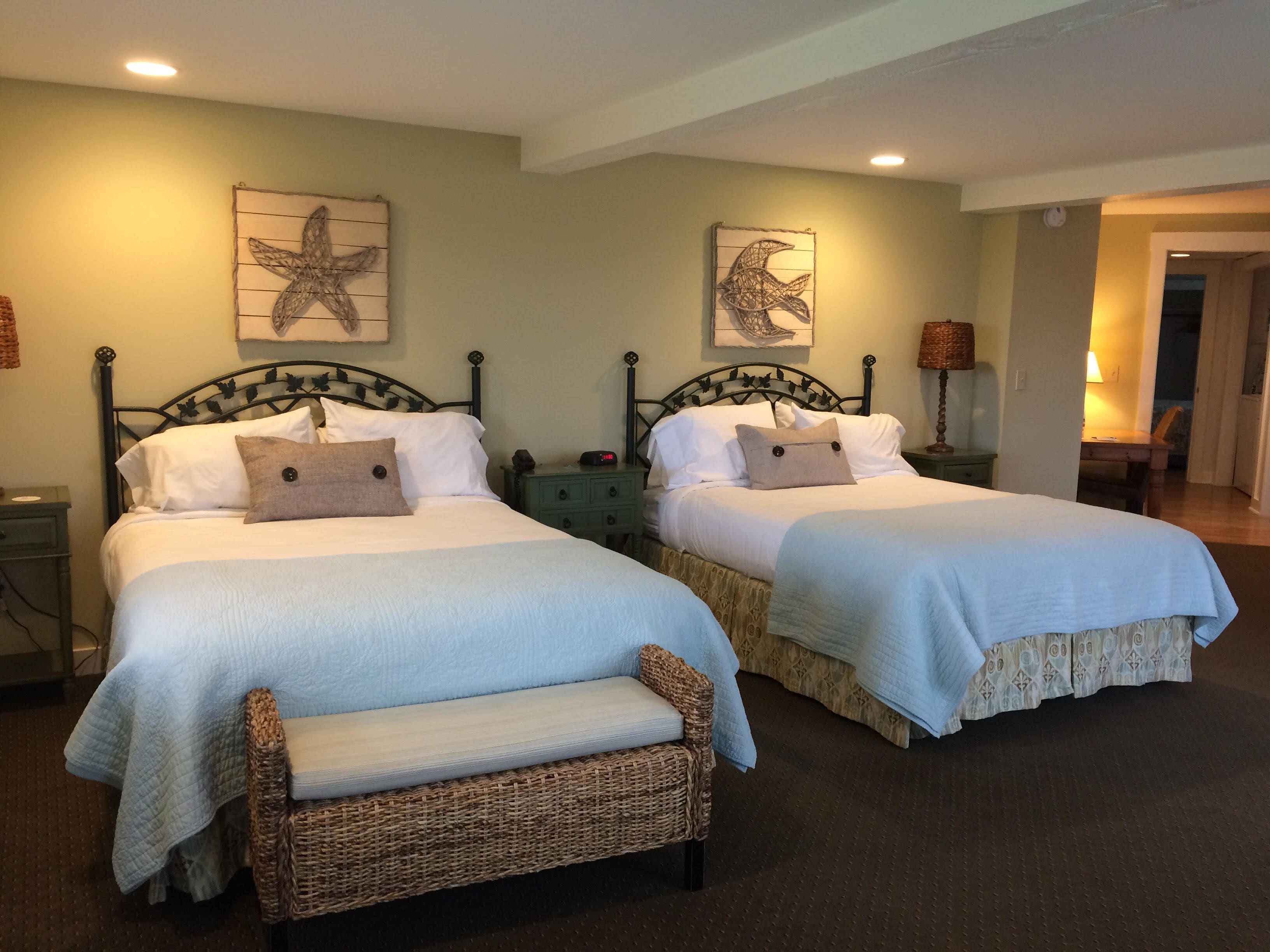A hotel room with two beds, each with a headboard, a bench, and artwork on the walls.
