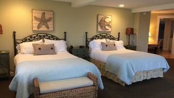 A hotel room with two beds, each with a headboard, a bench, and artwork on the walls.