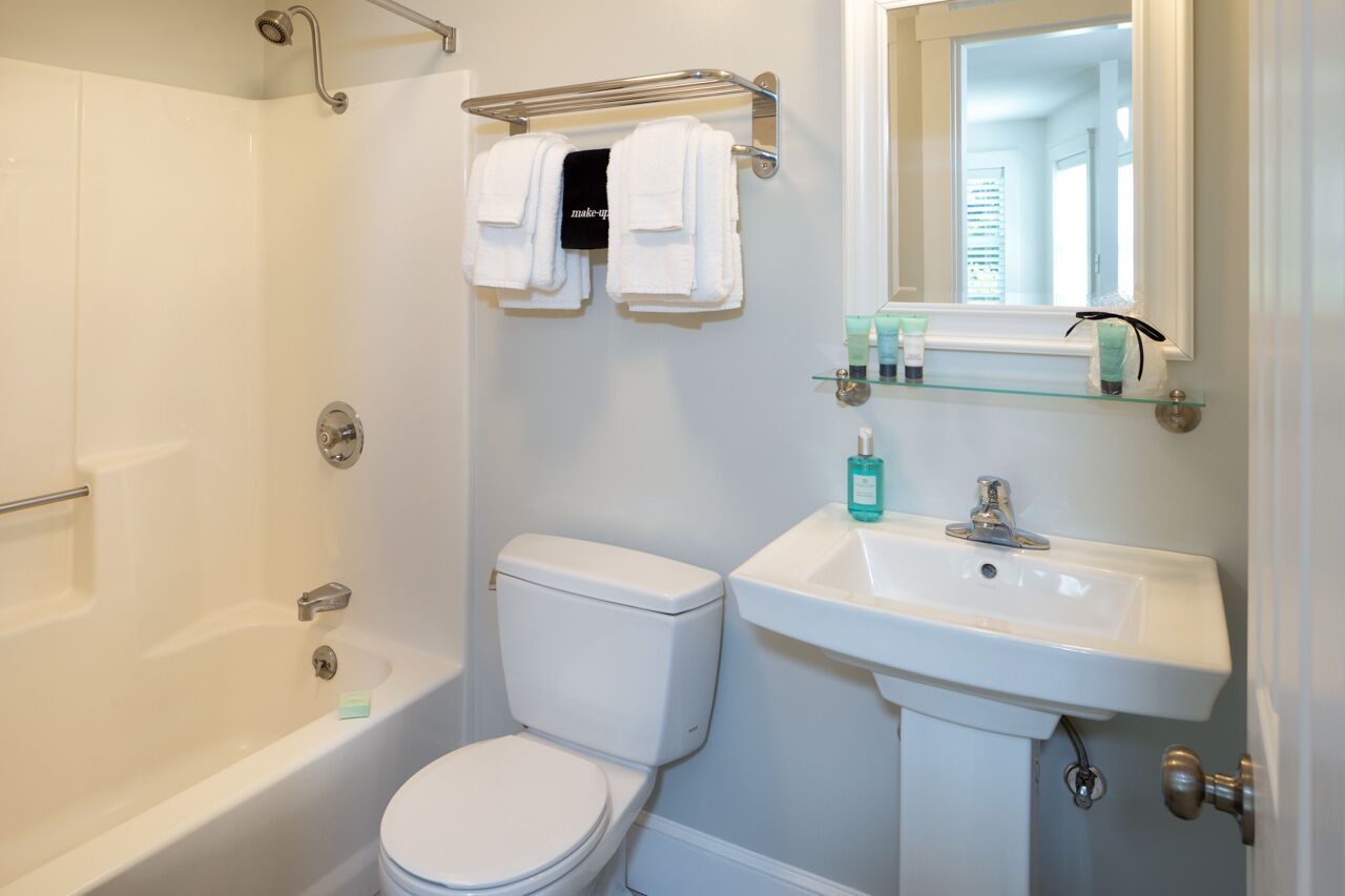 A bathroom with a bathtub, toilet, and sink. There are two white towels hanging on a rack above the toilet.