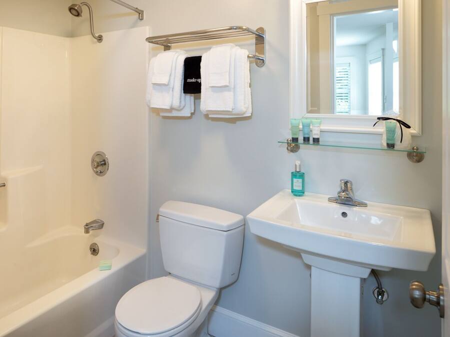 A bathroom with a bathtub, toilet, and sink. There are two white towels hanging on a rack above the toilet.