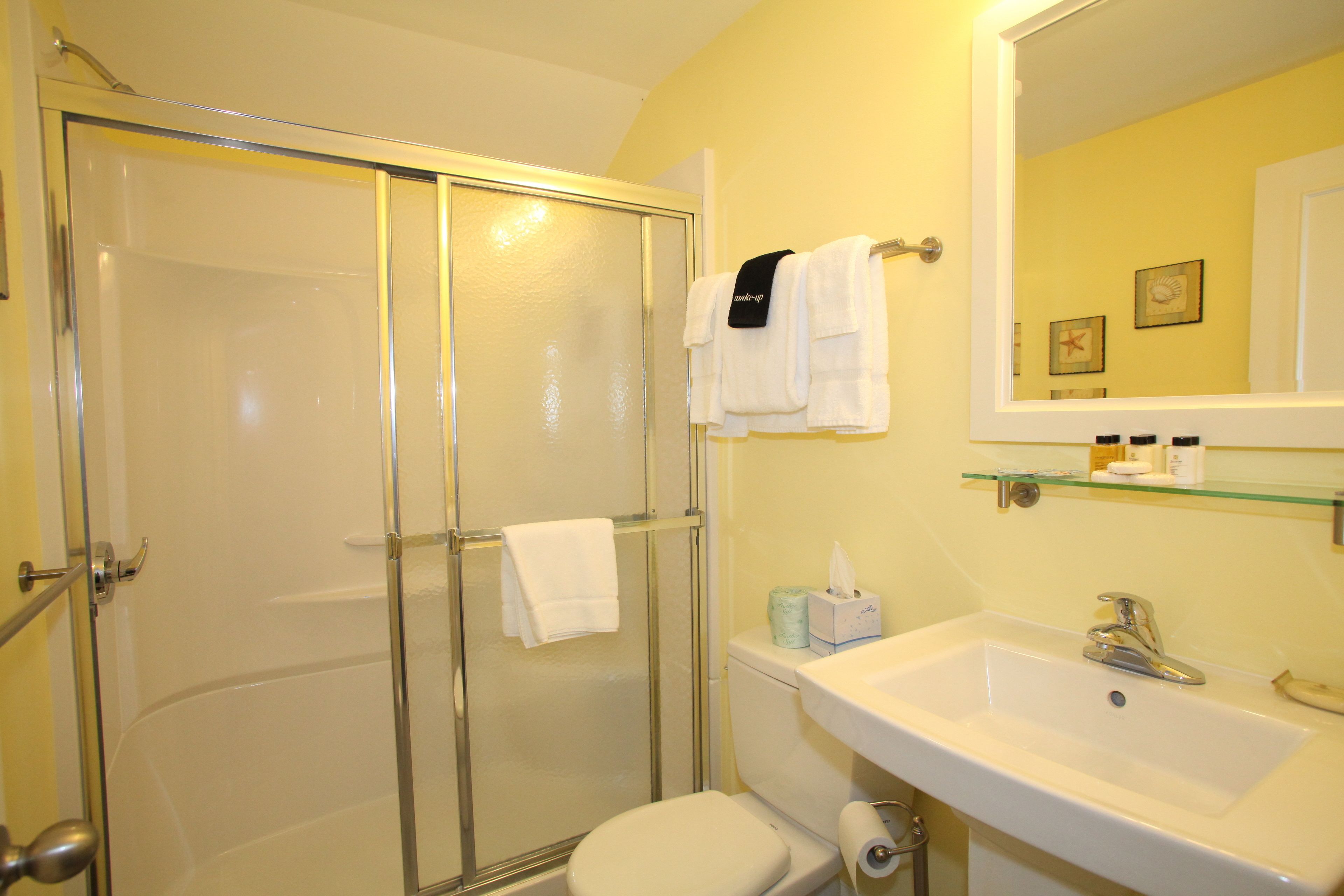 Un bany amb box de dutxa de vidre, vàter, un lavabo amb mirall i un suport de tovalloles amb tovalloles.