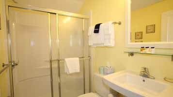 Ein Badezimmer mit Duschabtrennung aus Glas, Toilette, Waschbecken mit Spiegel und einem Handtuchhalter mit Handtüchern.