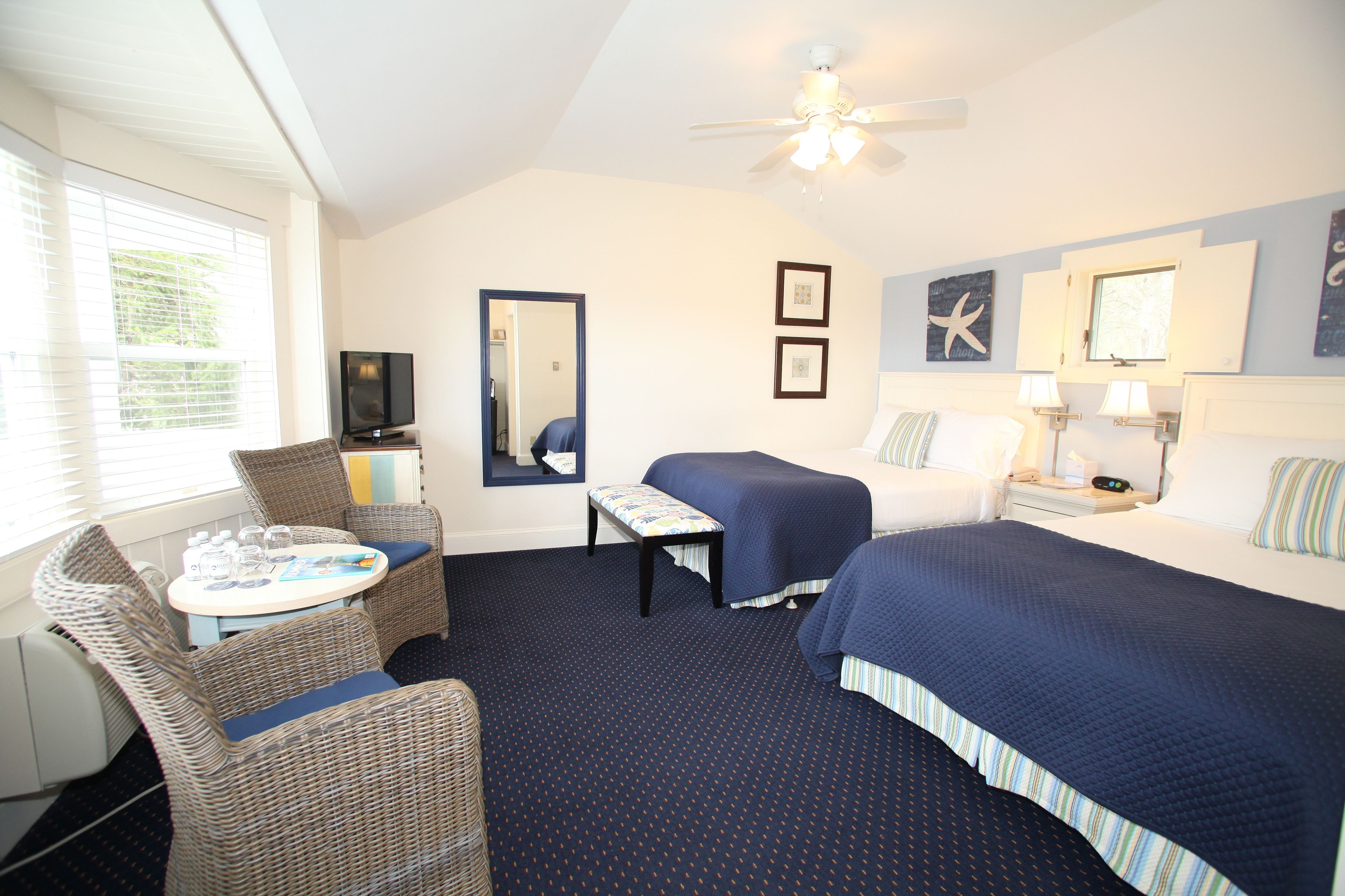 A hotel room with a bed, a chair, a small table, a ceiling fan, and a window with blinds.