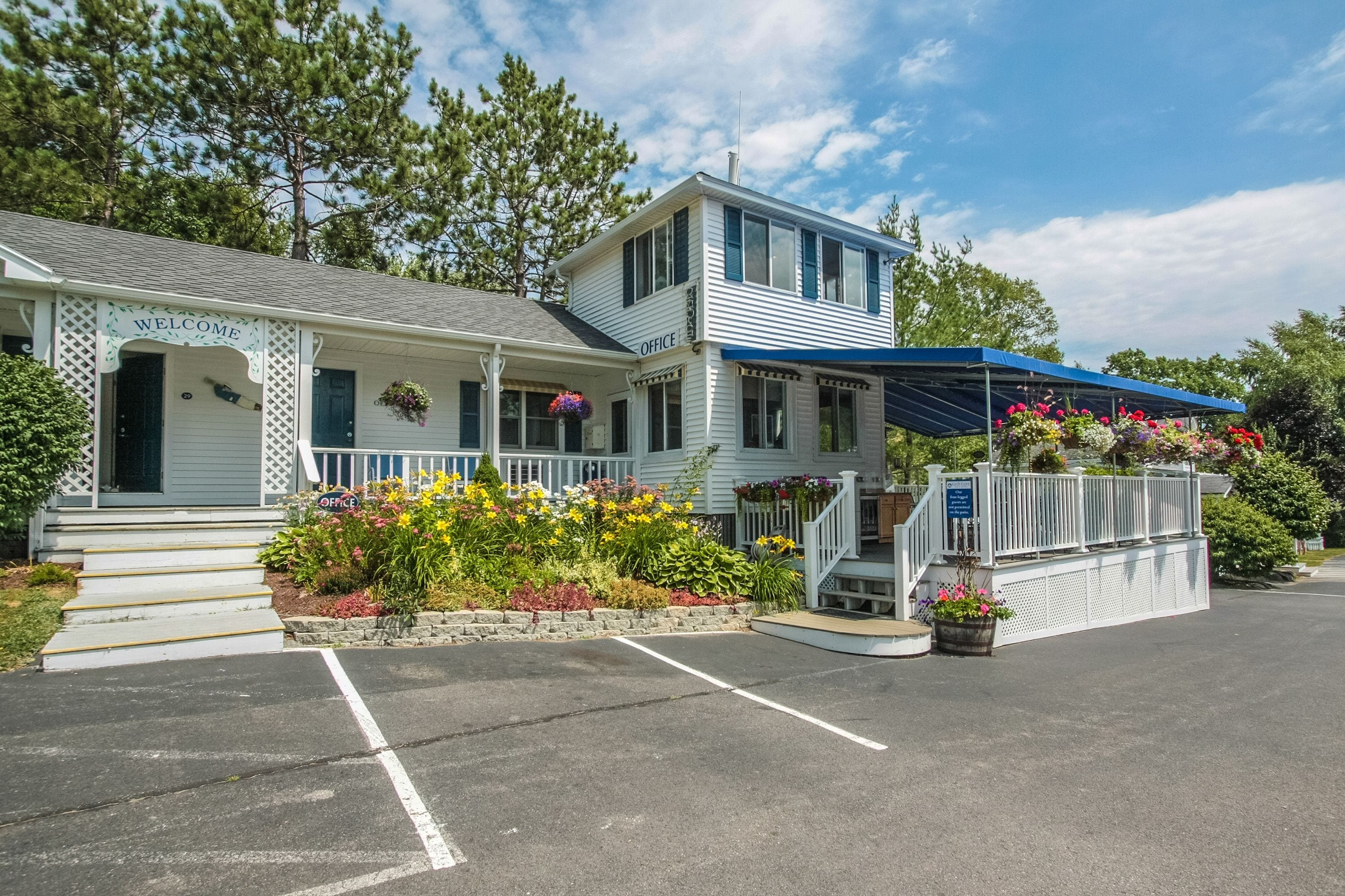 A two-story building with a 'Welcome' sign, an 'Office' sign, and a covered porch with hanging flower baskets.