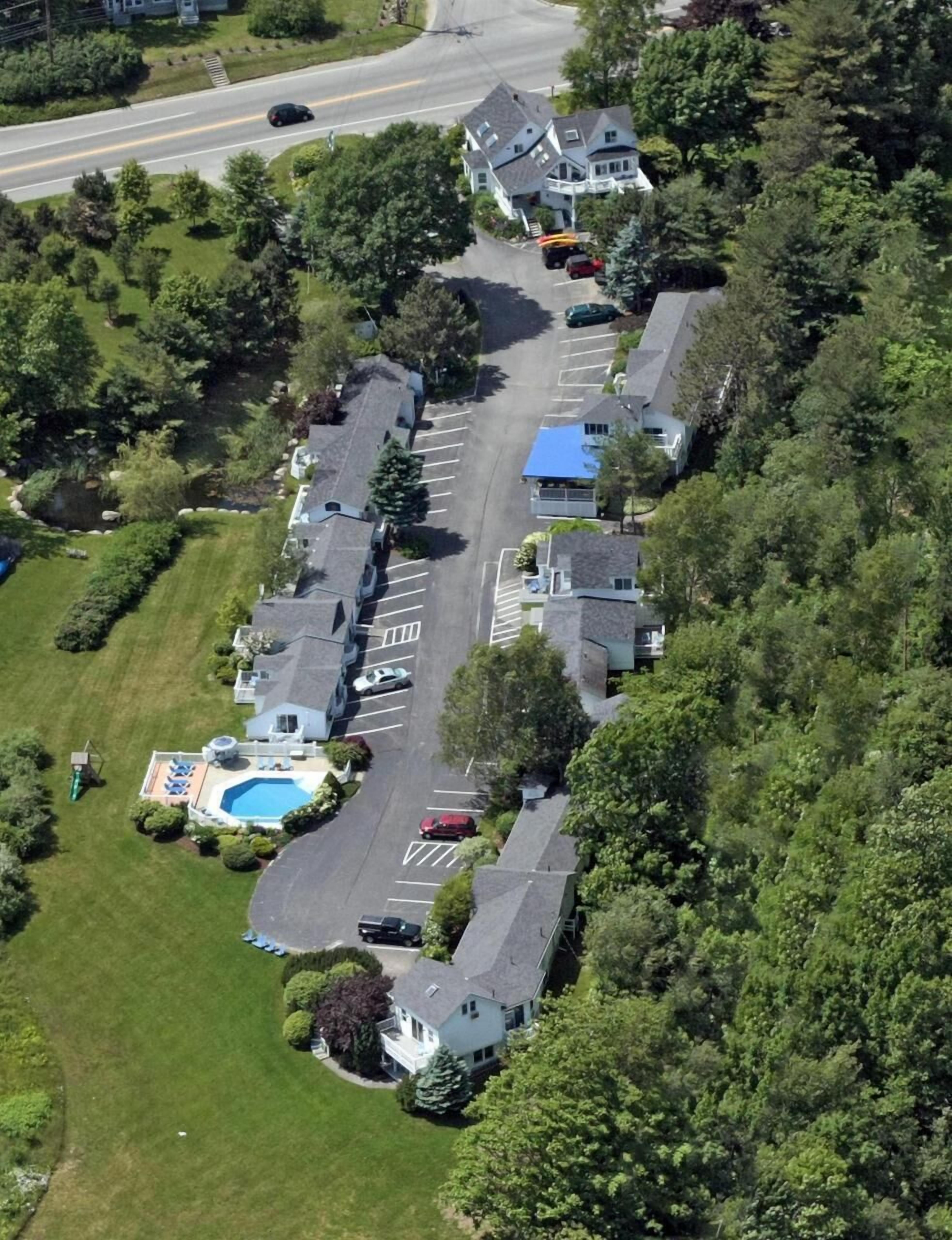 Vista aérea de una zona residencial con varias casas, una piscina y una carretera.