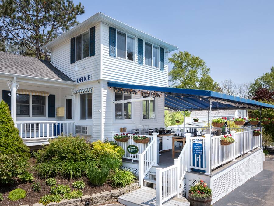 A white building with a blue awning, a deck with hanging flower baskets, and a sign indicating a coffee shop.