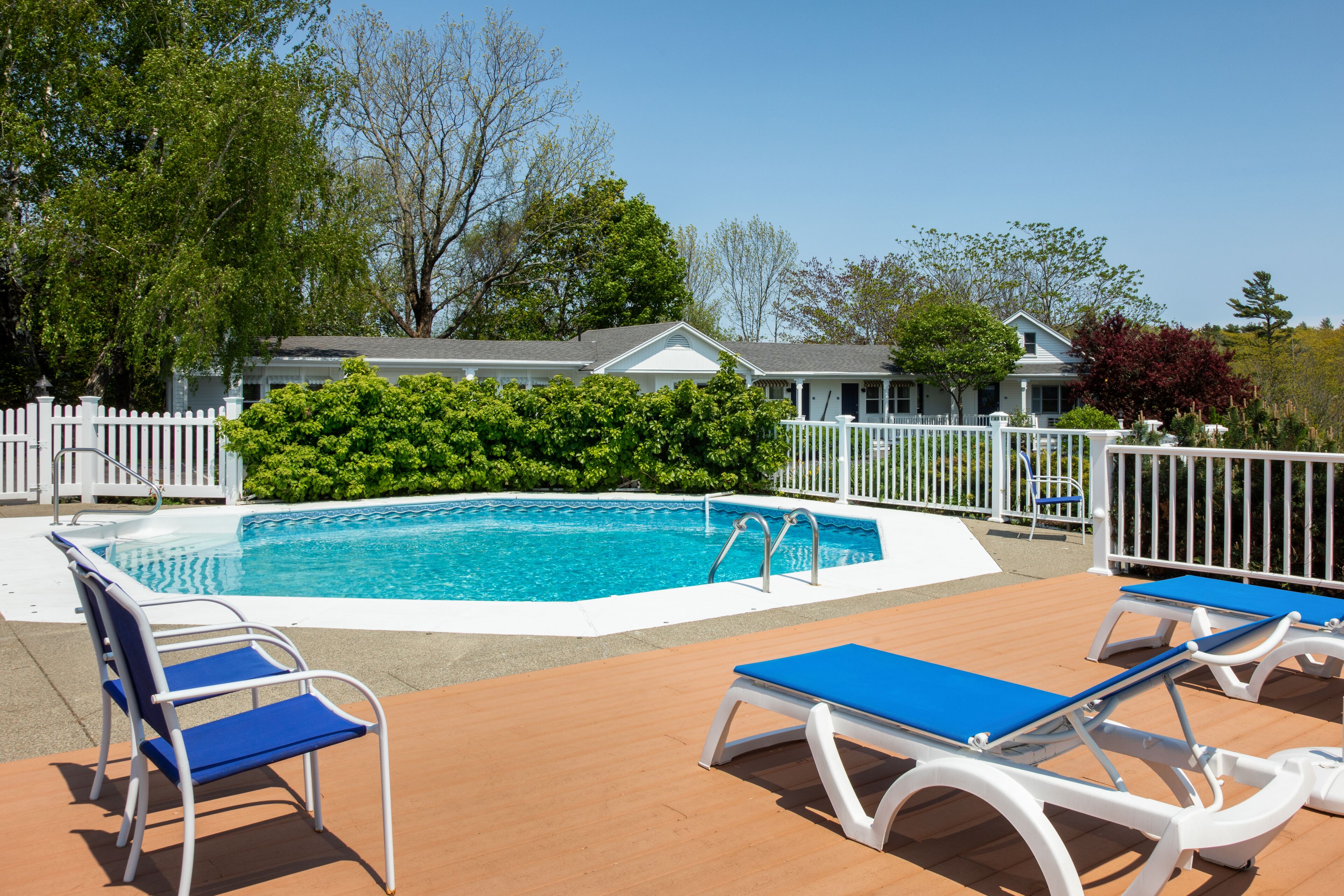 A swimming pool with lounge chairs and a white fence.