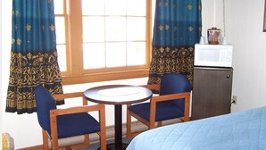 A hotel room with a bed, a small round table, two chairs, a microwave, and a cabinet. - Eastview Motel (Saco)