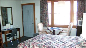 A hotel room with a bed, a desk with a chair, a small table with two chairs, a door, and a window with curtains. - Eastview Motel (Saco)