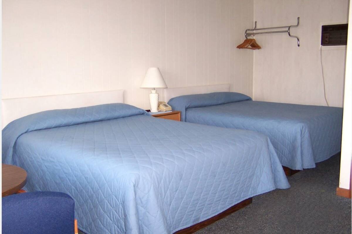 A room with two beds, a small table, a lamp, and a coat rack.