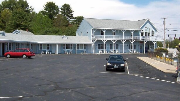 A motel with a large parking lot, a covered porch, and a blue building with white trim. - Eastview Motel (Saco)