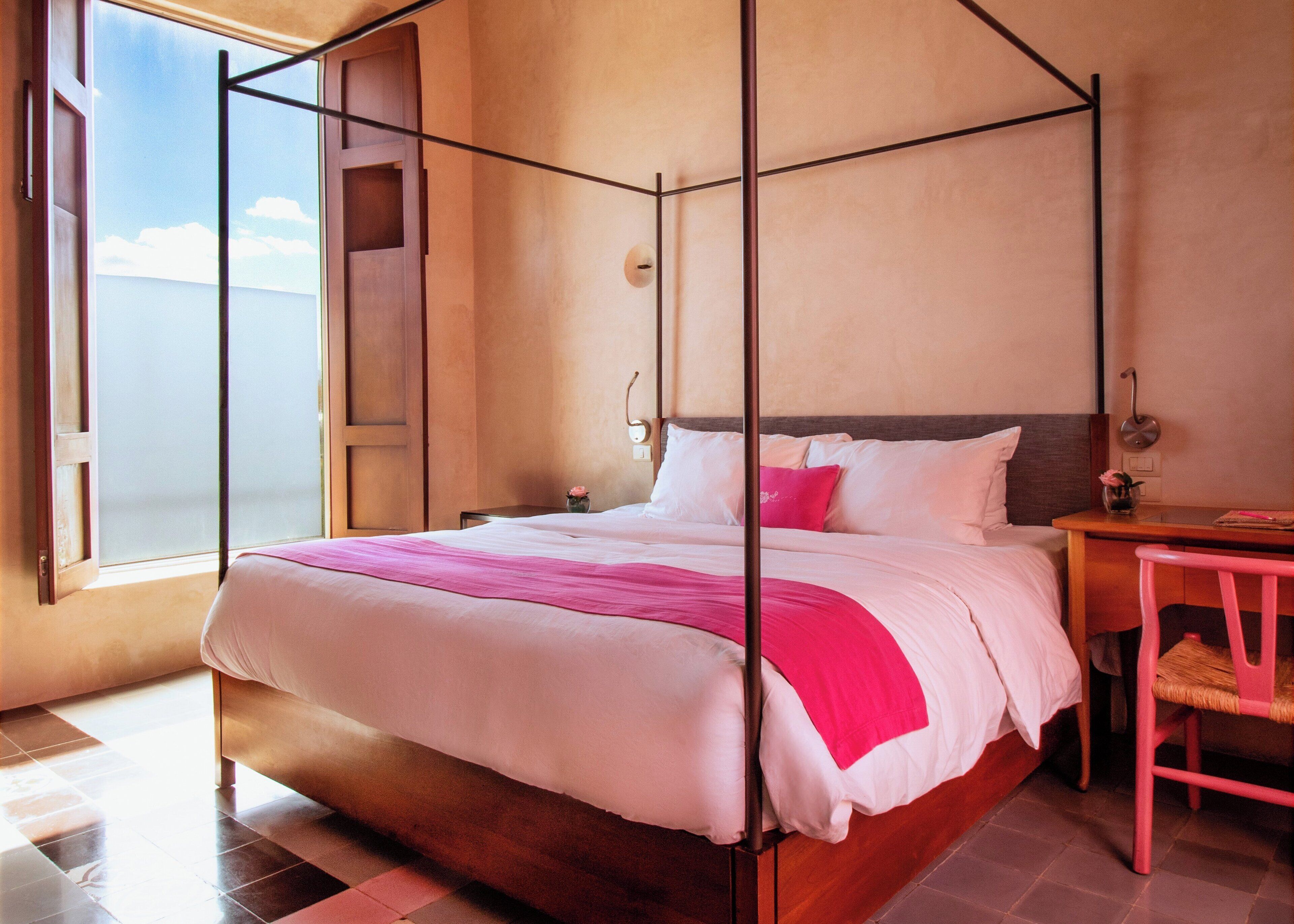 Una cama con dosel de madera, ropa de cama blanca y detalles en rosa.