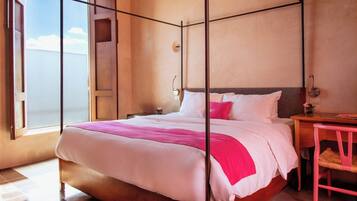 Una cama con dosel de madera, ropa de cama blanca y detalles en rosa.