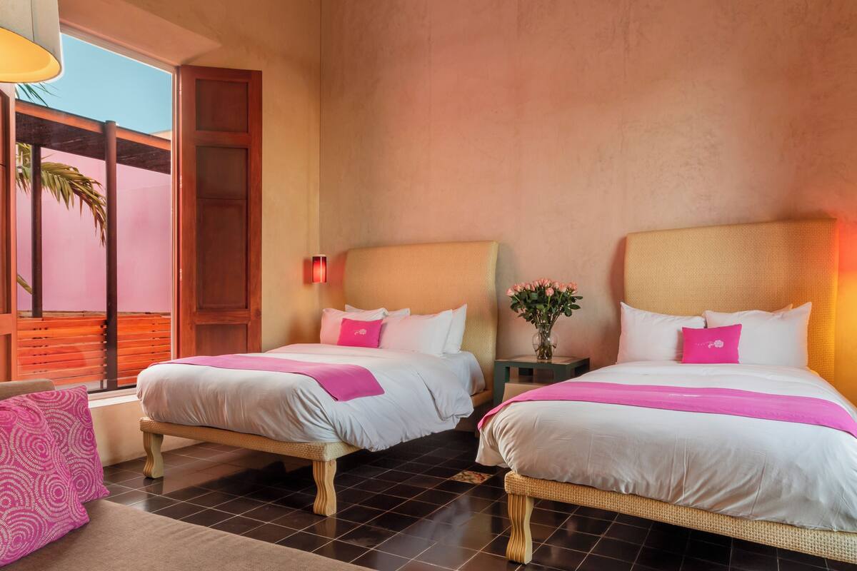 A hotel room with two beds, a view of palm trees, and a balcony.