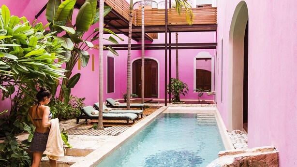 Zona de piscina con sillas de descanso y una persona de pie junto a la piscina.