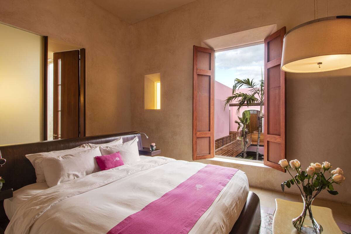 A hotel room with a bed, a nightstand, a vase with flowers, and a view of a balcony with plants.