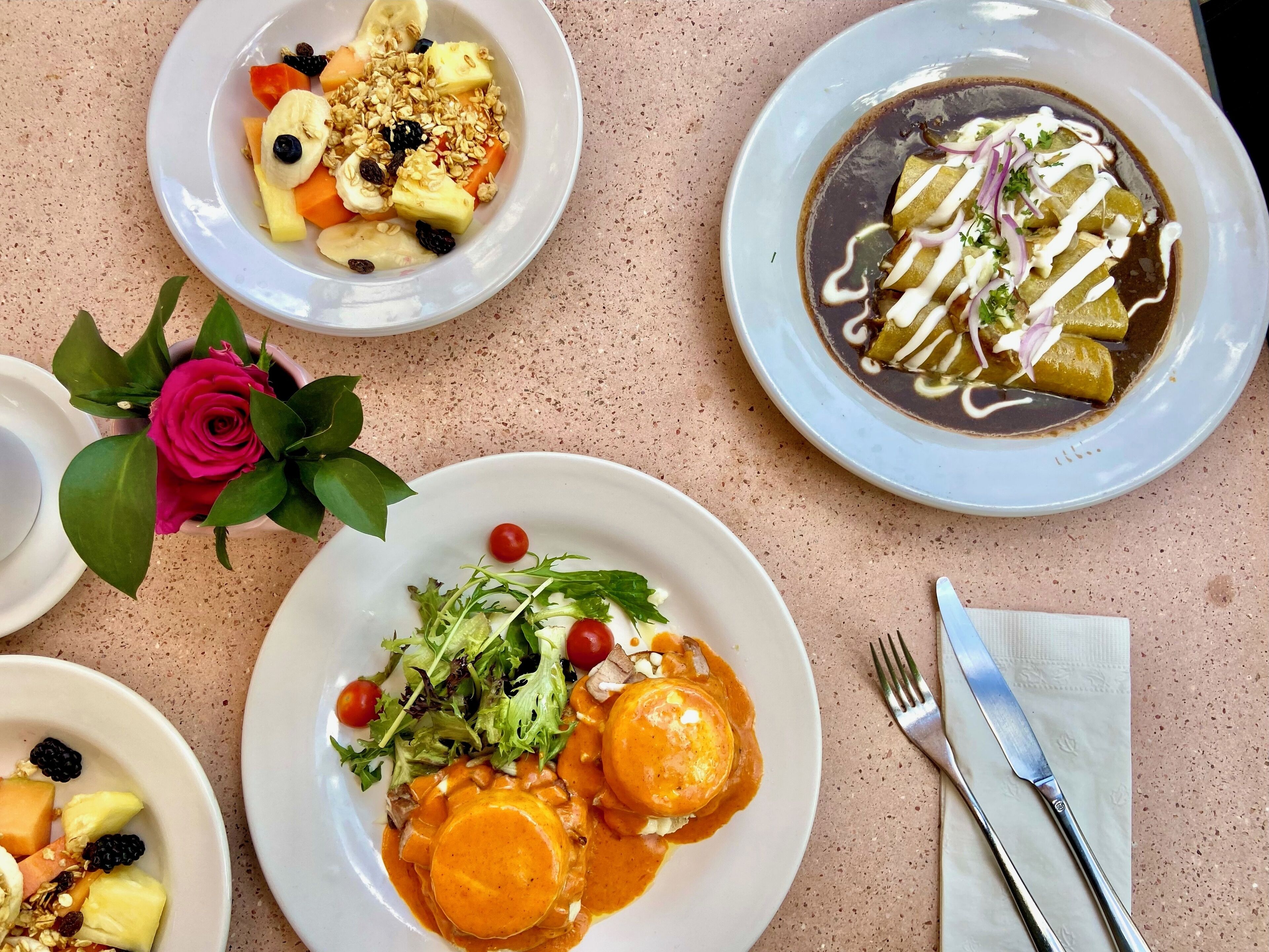 A table with various dishes, including a plate with enchiladas, a plate with fruit and granola, and a plate with a salad.
