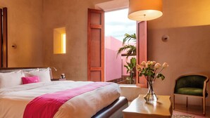 Habitación de hotel con una cama grande, una mesita de noche con un jarrón de flores, una silla verde y vistas al exterior.