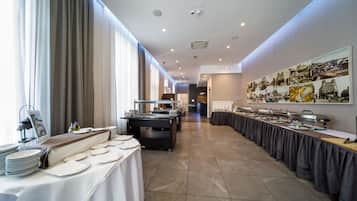 A modern hotel dining area with long tables, buffet stations, and a large cityscape mural on the wall.