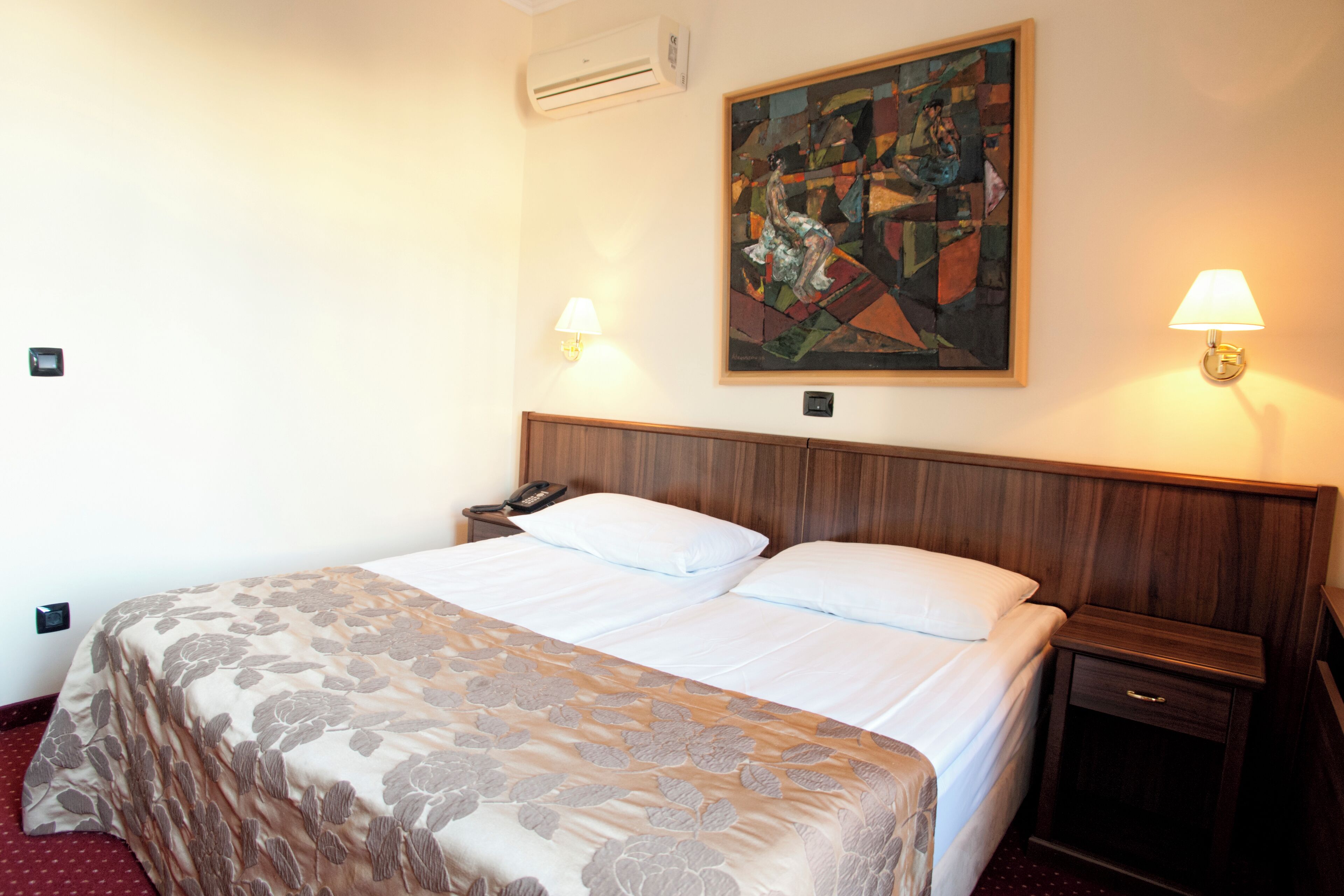 Habitación de hotel con una cama grande, una mesita de noche, un teléfono y dos lámparas fijadas a la pared.