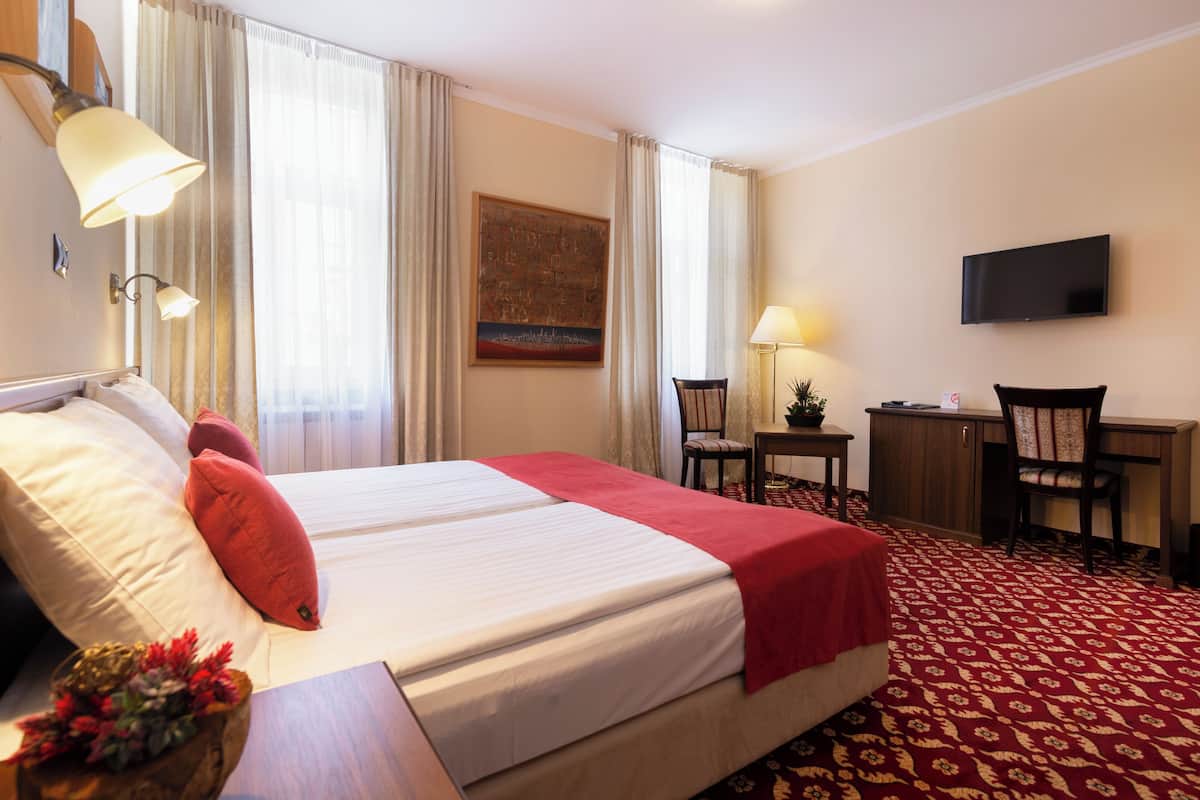 Una habitación de hotel con una cama grande, un escritorio, una silla, un televisor y un cuadro en la pared.