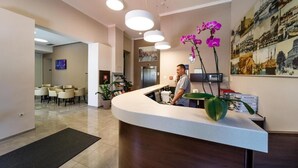 A hotel reception area with a curved reception desk, a man standing behind it, and a large poster of cityscapes on the wall. - Hotel Continental (Rijeka)
