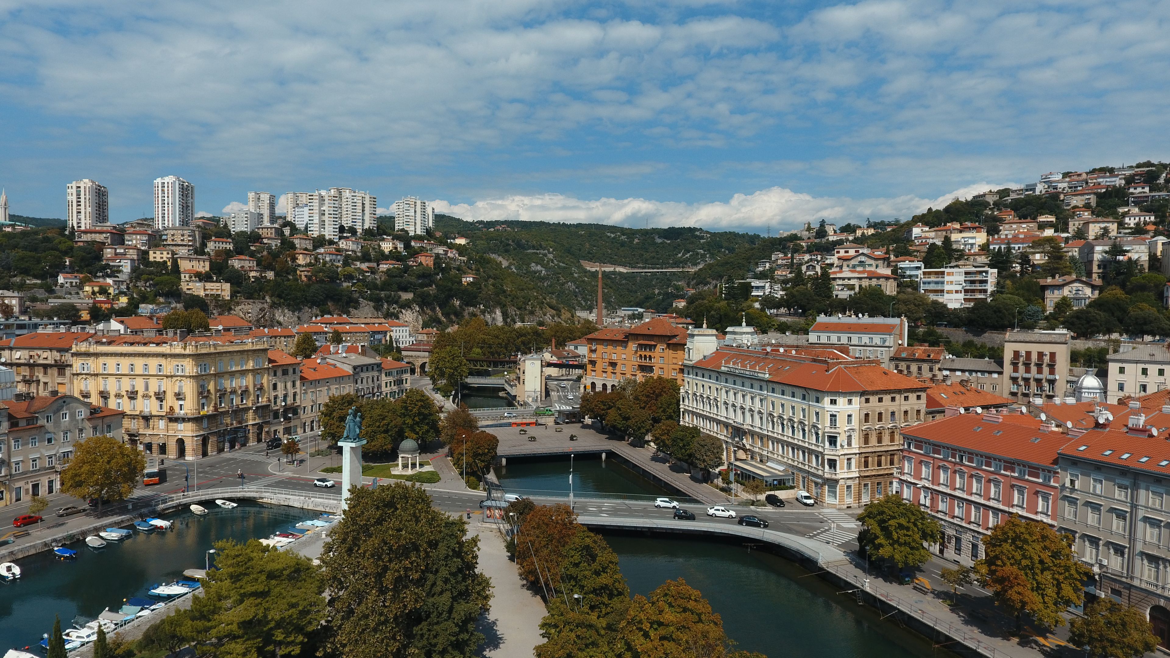 A riverside cityscape with historic buildings, a statue, and a bridge.
