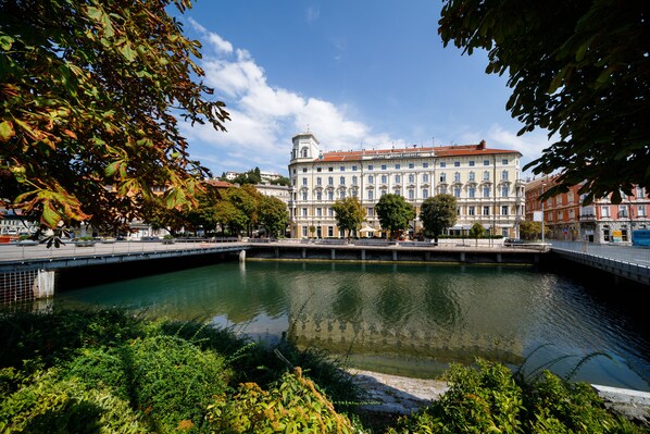 A historic building with classical architecture, a bridge, and a calm water body in the foreground.