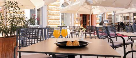 An outdoor café with tables and chairs, a potted plant, and umbrellas.