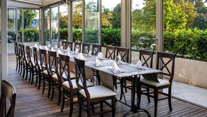 A restaurant with a long table set for dining, large windows, and a view of greenery. - Hotel Continental (Rijeka)