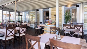 A restaurant with wooden tables and chairs, a central bar area with a fruit basket, and large windows allowing natural light. - Hotel Continental (Rijeka)