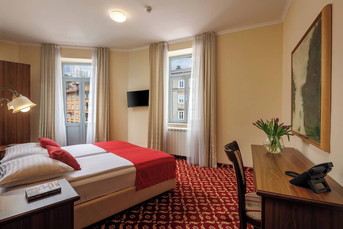Una habitación de hotel con cama, escritorio, silla, televisor y ventana con cortinas.