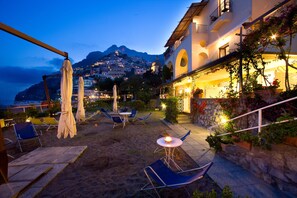 Una terraza con mobiliario exterior, un muro de piedra con plantas y una vista de montaña al fondo.