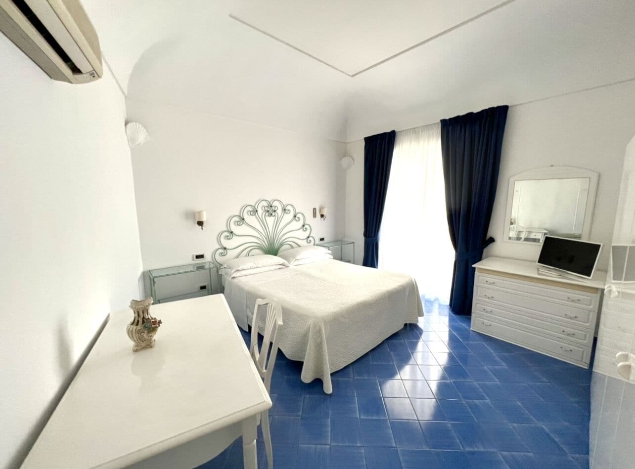 A bedroom with a bed, a desk, a dresser, and a mirror.