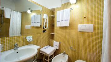 Un baño con paredes de azulejos amarillos, dos lavamanos, un bidé y varias toallas blancas con texto.