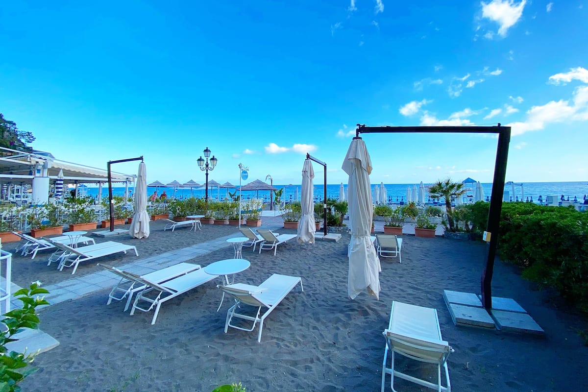 A beachside patio with sun loungers, umbrellas, and potted plants.