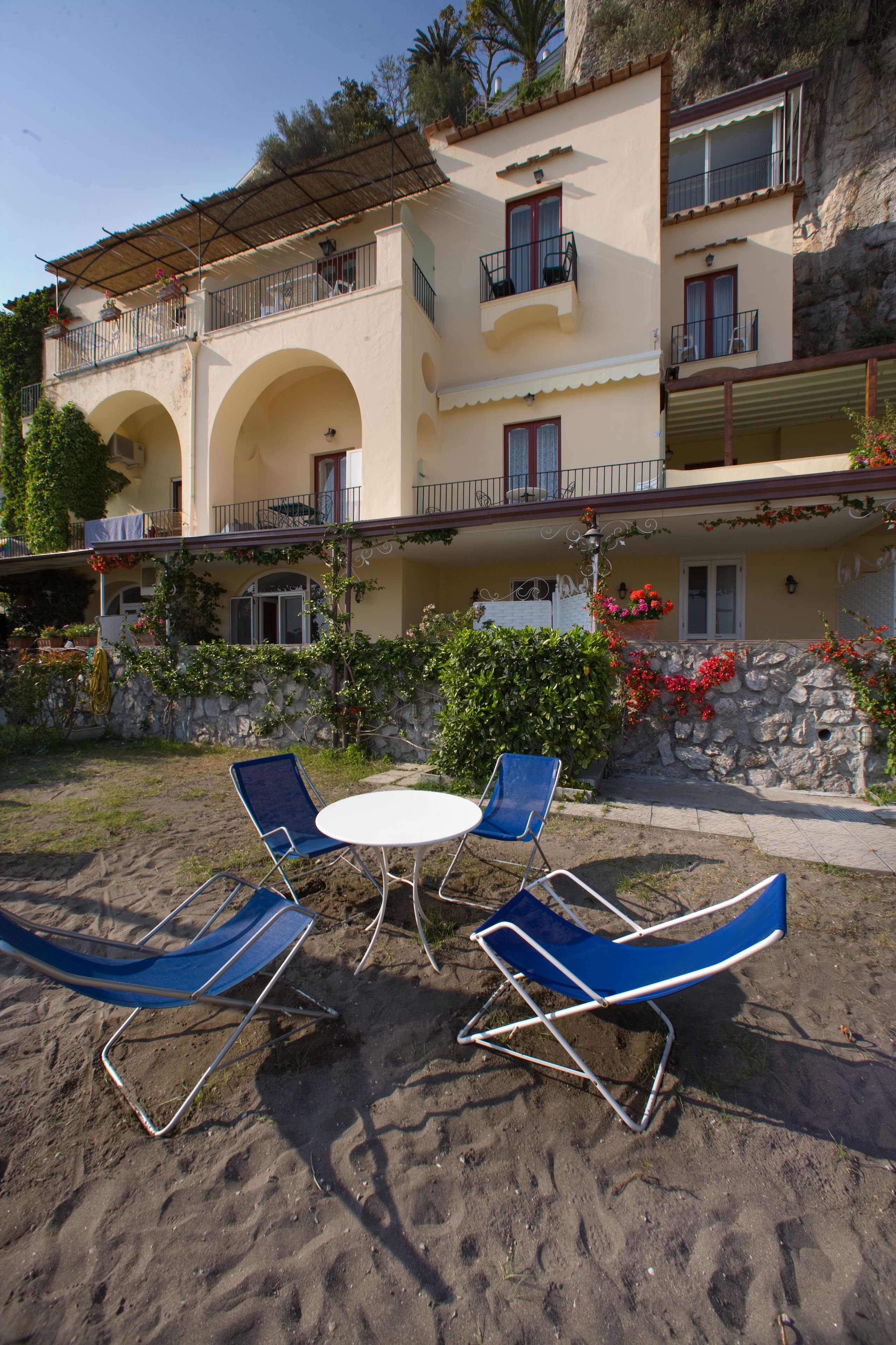 A building with a balcony, a stone wall, and a garden with flowers and plants.
