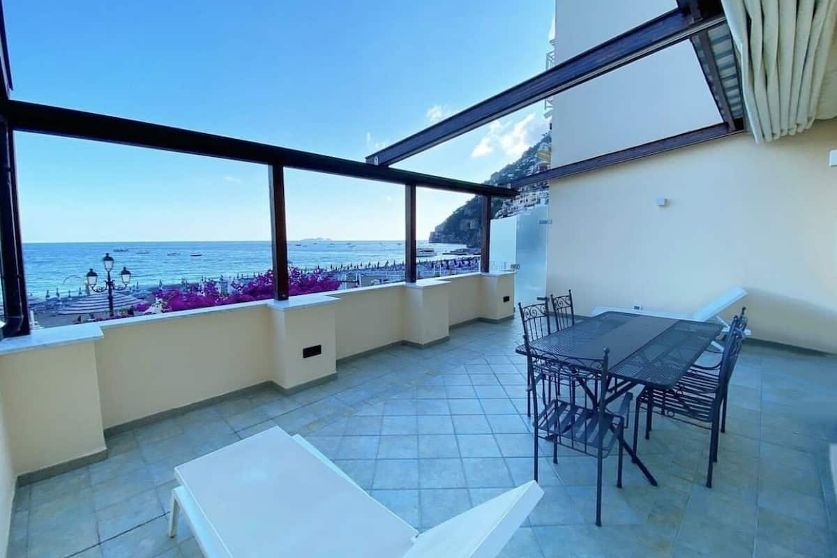 A rooftop terrace with a table and chairs, a white bench, and a view of the sea.